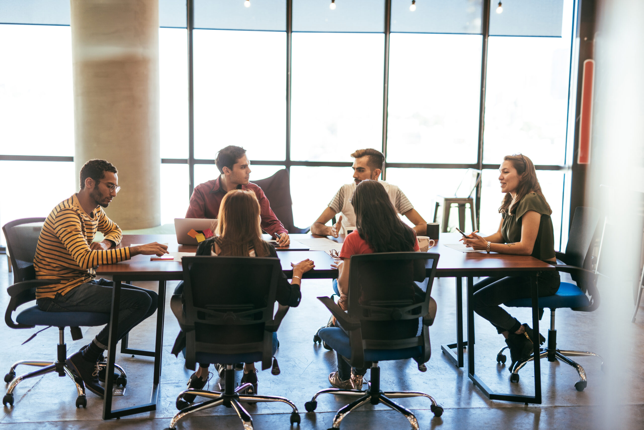 Group of business people sitting at a large table, holding a meeting in a brightly lit room