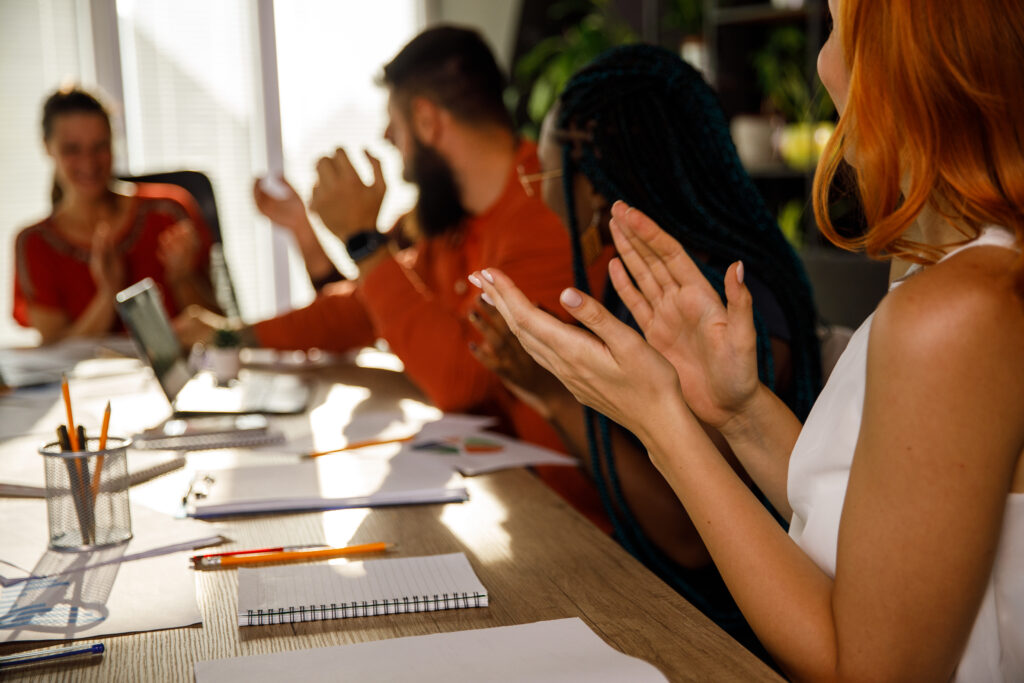 Group of business people sitting at a large table with notebooks and pencils clapping